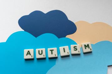 Scrabble tiles spell out the word Autism upon a background made of cut out paper clouds
